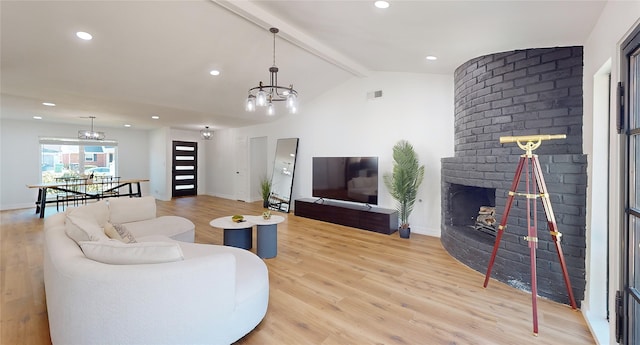 living room featuring lofted ceiling with beams, a brick fireplace, light wood-type flooring, and an inviting chandelier