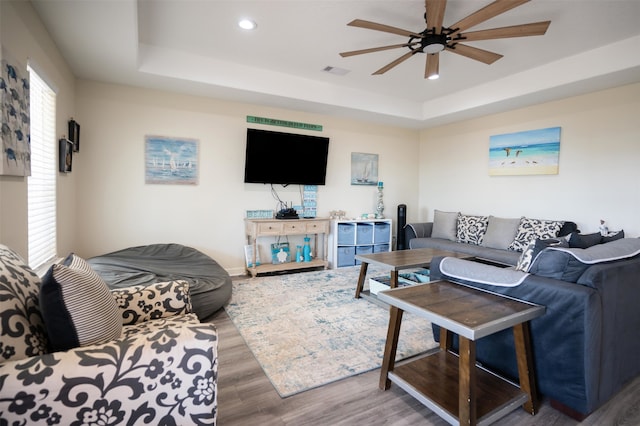 living room featuring ceiling fan, wood-type flooring, and a tray ceiling