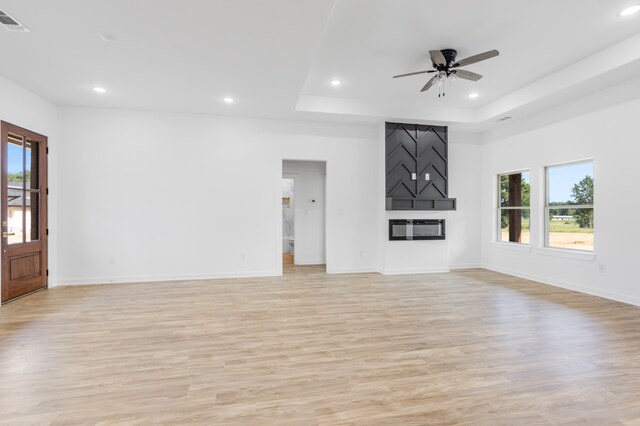 unfurnished living room featuring a tray ceiling, light wood-type flooring, and ceiling fan