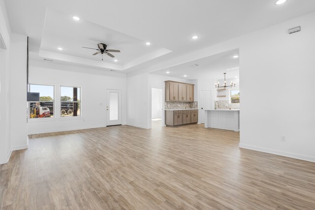 unfurnished living room featuring a raised ceiling, light hardwood / wood-style flooring, and ceiling fan with notable chandelier