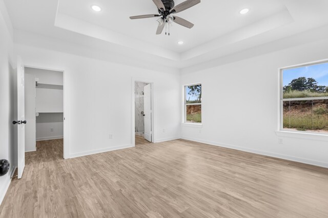 unfurnished bedroom with ensuite bathroom, multiple windows, a walk in closet, and light wood-type flooring