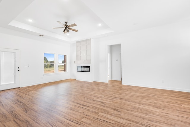 unfurnished living room featuring a tray ceiling, ceiling fan, and light wood-type flooring