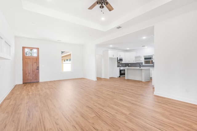 unfurnished living room with light hardwood / wood-style floors, a raised ceiling, and ceiling fan