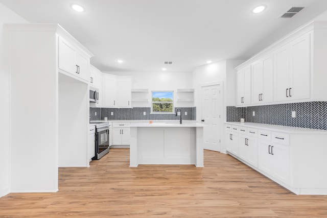 kitchen with appliances with stainless steel finishes, sink, white cabinets, light hardwood / wood-style floors, and an island with sink