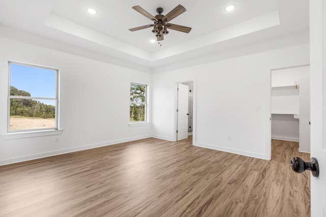 unfurnished bedroom with a walk in closet, a tray ceiling, and ceiling fan