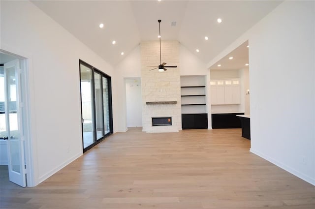 unfurnished living room with ceiling fan, a stone fireplace, high vaulted ceiling, and plenty of natural light