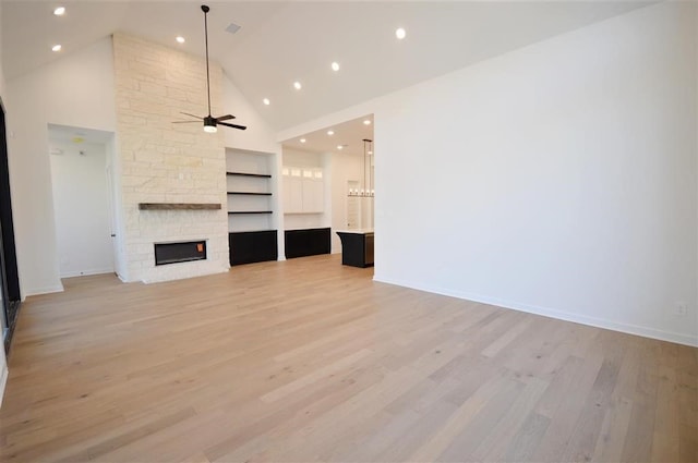 unfurnished living room with light wood-type flooring, high vaulted ceiling, built in features, ceiling fan, and a stone fireplace