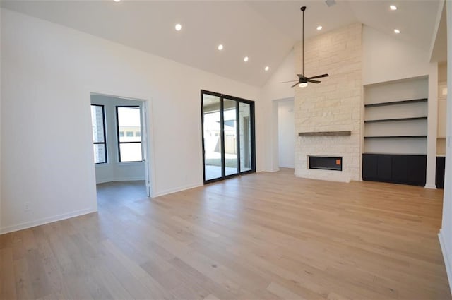 unfurnished living room with a stone fireplace, ceiling fan, high vaulted ceiling, light hardwood / wood-style flooring, and built in features