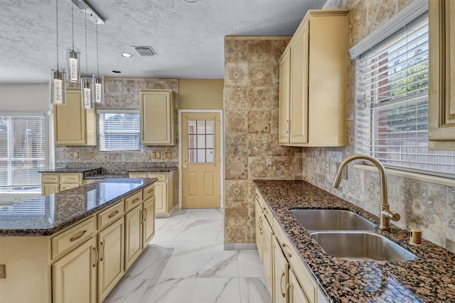 kitchen with dark stone counters, a textured ceiling, sink, decorative light fixtures, and a kitchen island