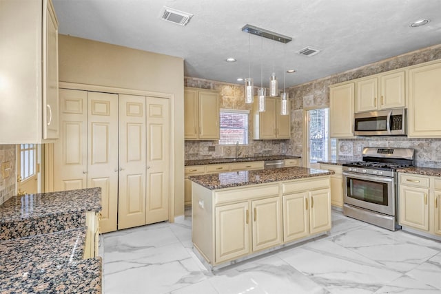 kitchen with sink, a center island, dark stone counters, pendant lighting, and stainless steel appliances