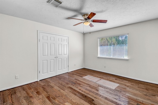 unfurnished bedroom with ceiling fan, hardwood / wood-style floors, a closet, and a textured ceiling