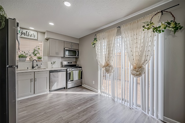 kitchen featuring decorative backsplash, a textured ceiling, sink, light hardwood / wood-style floors, and stainless steel appliances