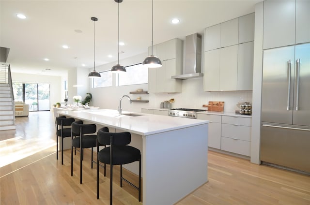 kitchen with hanging light fixtures, wall chimney exhaust hood, an island with sink, a kitchen bar, and stainless steel built in refrigerator