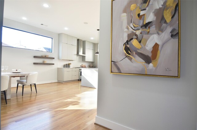 kitchen featuring light wood-type flooring, wall chimney exhaust hood, decorative light fixtures, stainless steel range oven, and white cabinets