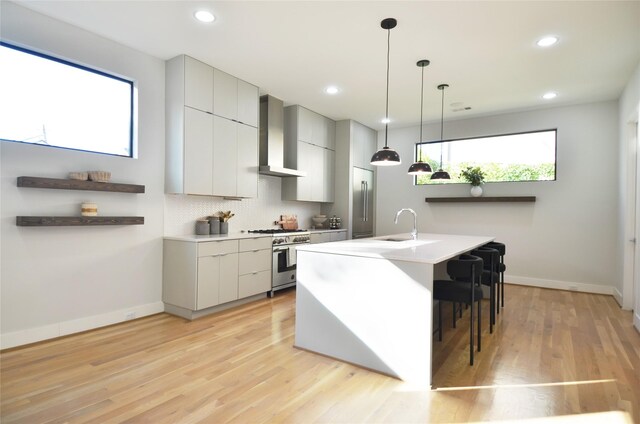 kitchen featuring backsplash, light hardwood / wood-style floors, high quality appliances, and wall chimney range hood