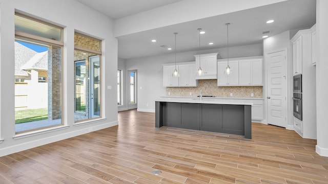 kitchen featuring backsplash, pendant lighting, white cabinetry, an island with sink, and stainless steel appliances