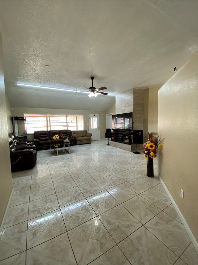 living room with ceiling fan, light tile patterned flooring, a textured ceiling, and lofted ceiling