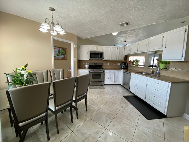 kitchen with appliances with stainless steel finishes, white cabinetry, a textured ceiling, vaulted ceiling, and a notable chandelier