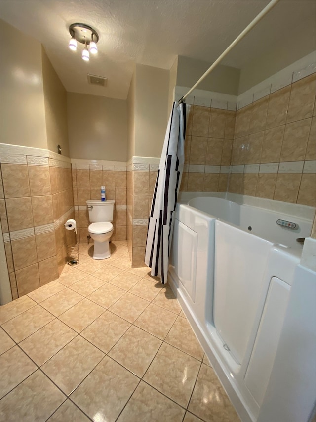 bathroom with toilet, tile walls, a textured ceiling, and tile patterned flooring