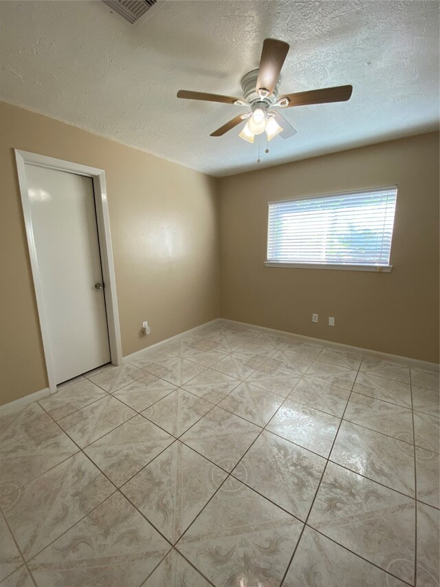 unfurnished room featuring a textured ceiling, light tile patterned floors, and ceiling fan