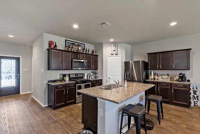 kitchen with an island with sink, light stone countertops, a kitchen bar, dark hardwood / wood-style floors, and stainless steel appliances