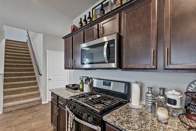 kitchen featuring light stone countertops, stainless steel appliances, wood-type flooring, and dark brown cabinets