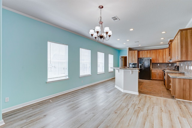 kitchen with light hardwood / wood-style flooring, black appliances, crown molding, and an island with sink