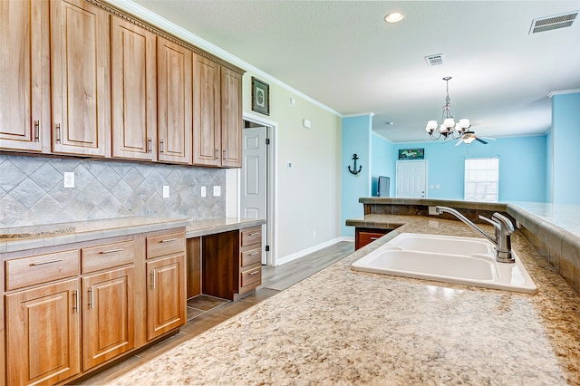 kitchen with sink, backsplash, decorative light fixtures, crown molding, and an inviting chandelier