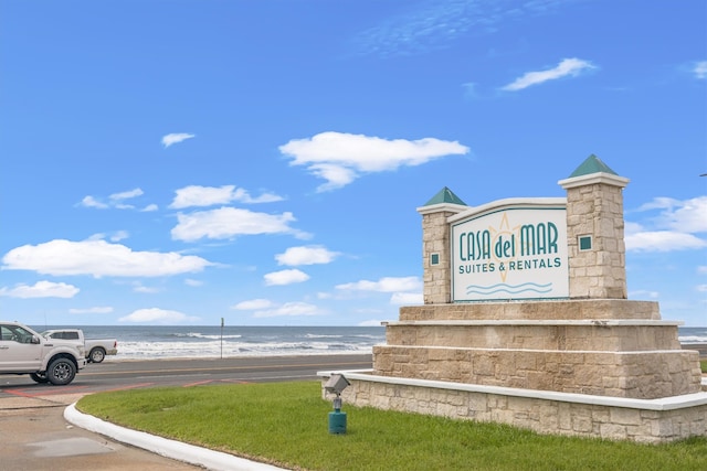 community sign featuring a water view and a view of the beach