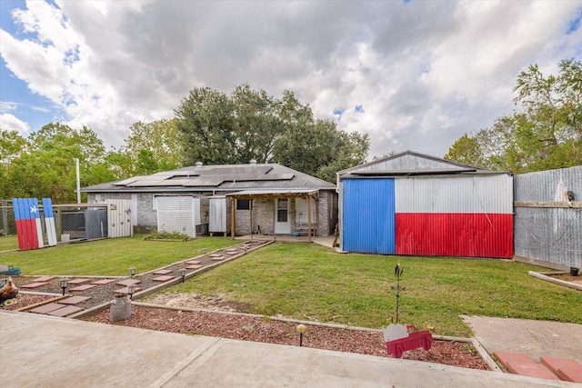 back of house with an outdoor structure, a yard, brick siding, fence, and solar panels