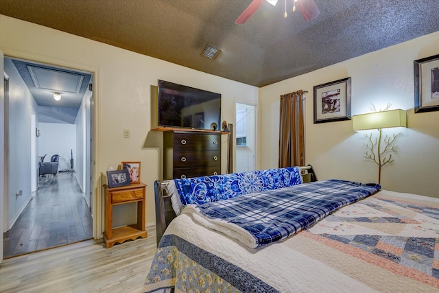 bedroom with wood finished floors, attic access, baseboards, visible vents, and a textured ceiling