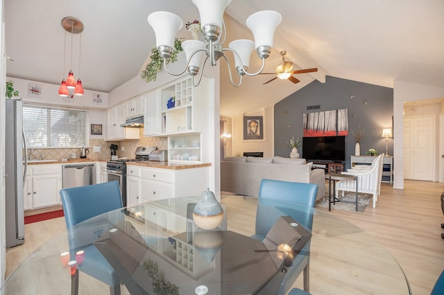 dining room featuring lofted ceiling, light hardwood / wood-style flooring, a fireplace, and ceiling fan