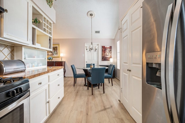 kitchen featuring light hardwood / wood-style flooring, hanging light fixtures, vaulted ceiling, white cabinets, and appliances with stainless steel finishes