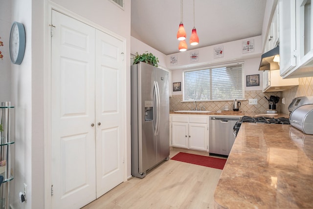 kitchen featuring exhaust hood, pendant lighting, white cabinetry, appliances with stainless steel finishes, and light hardwood / wood-style floors