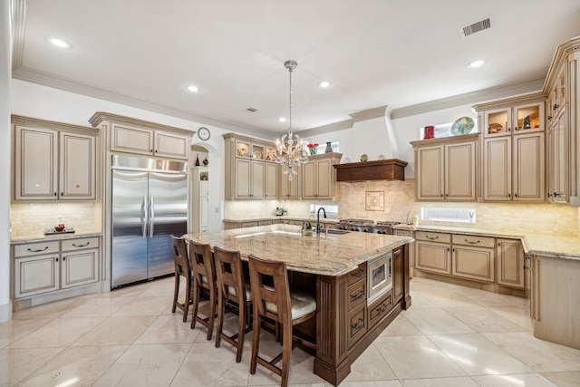 kitchen featuring premium range hood, ornamental molding, a kitchen island with sink, and built in appliances