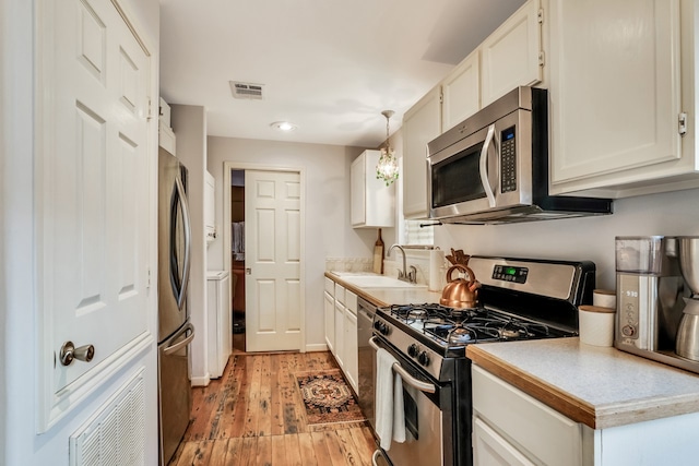 kitchen featuring sink, stainless steel appliances, pendant lighting, white cabinets, and light hardwood / wood-style flooring