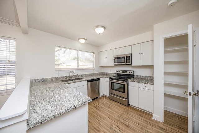 kitchen featuring sink, light wood-type flooring, kitchen peninsula, stainless steel appliances, and white cabinets