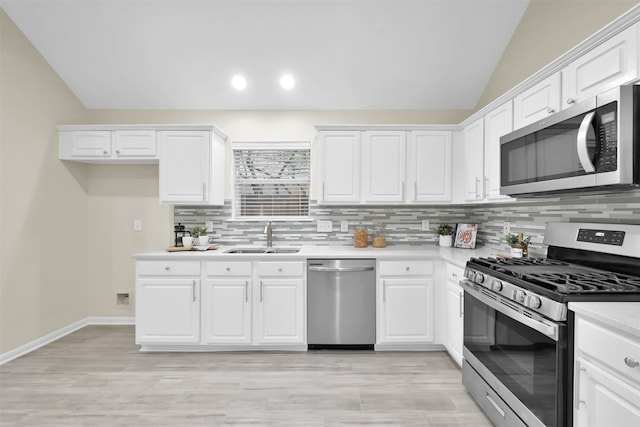 kitchen featuring stainless steel appliances, backsplash, sink, vaulted ceiling, and white cabinetry