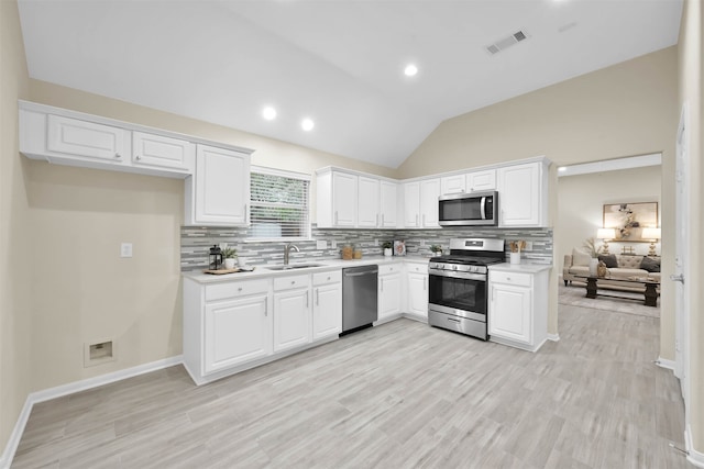 kitchen featuring appliances with stainless steel finishes, lofted ceiling, white cabinetry, and sink