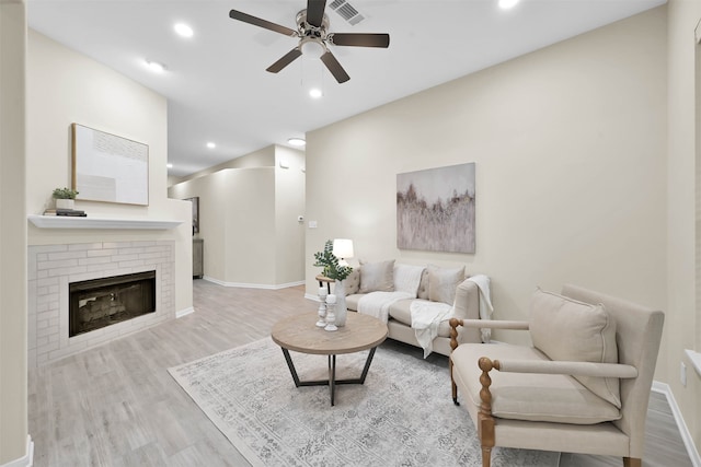 living room featuring ceiling fan, light wood-type flooring, and a fireplace