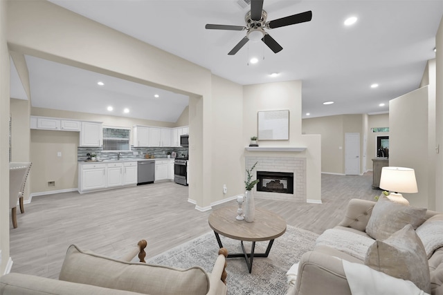 living room with light hardwood / wood-style floors, ceiling fan, vaulted ceiling, and a brick fireplace