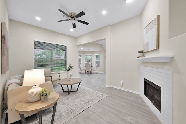 living room with light hardwood / wood-style floors, ceiling fan, and a brick fireplace