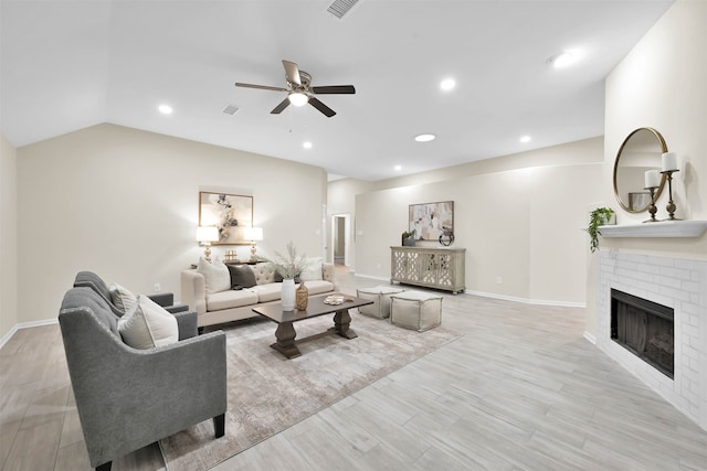 living room featuring vaulted ceiling, light hardwood / wood-style flooring, a fireplace, and ceiling fan