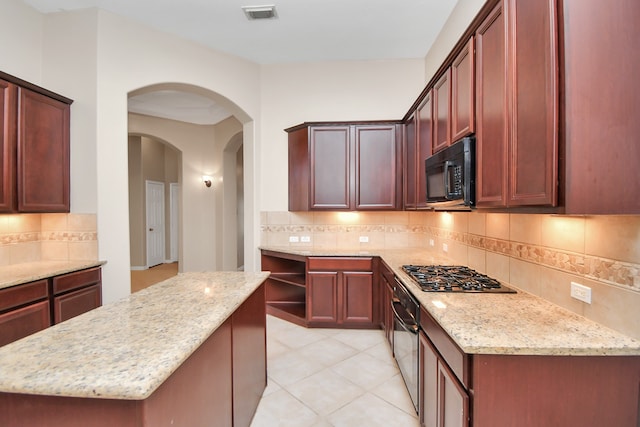 kitchen featuring appliances with stainless steel finishes, backsplash, a center island, light stone counters, and light tile patterned floors