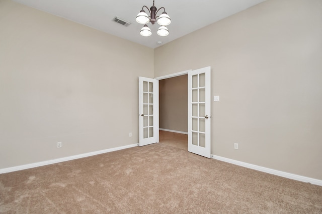 spare room with french doors, light colored carpet, and a notable chandelier