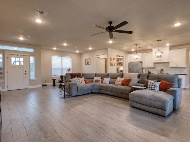 living room with a textured ceiling, light wood-type flooring, and ceiling fan