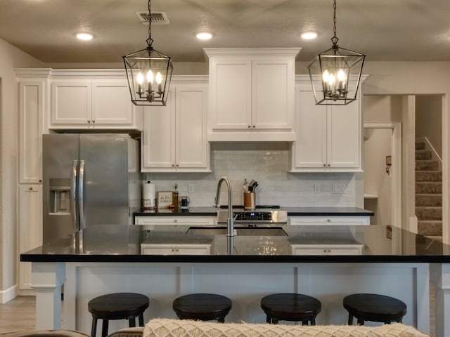 kitchen with a center island with sink, hanging light fixtures, white cabinetry, and a breakfast bar area