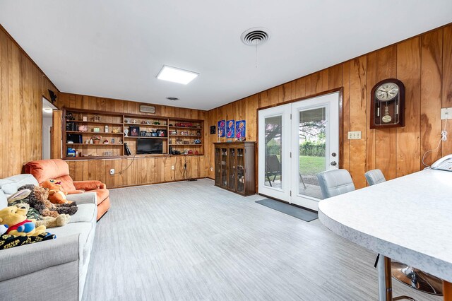 living room featuring built in shelves, wooden walls, and light hardwood / wood-style floors