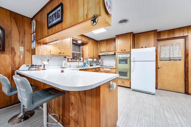 kitchen featuring a breakfast bar, sink, light wood-type flooring, kitchen peninsula, and white appliances