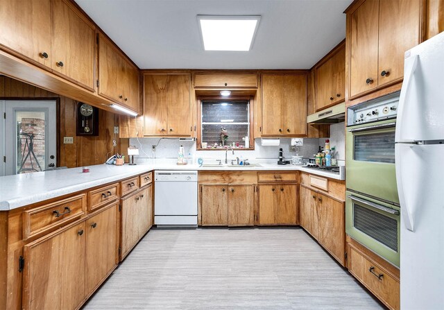 kitchen featuring sink, white appliances, kitchen peninsula, and backsplash